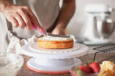 A layer cake being frosted on a rotating turntable