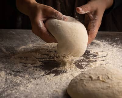 Hands shaping a taut round of bread dough on a floured counter