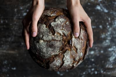 Hands holding a rustic loaf baked with reclaimed grains